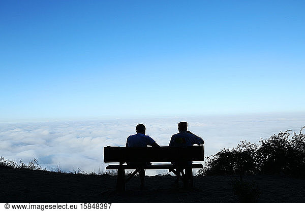 two men on park bench on mountain top overlooking clouds