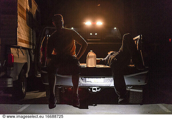 two men resting sitting back of truck backlit in the night water jug
