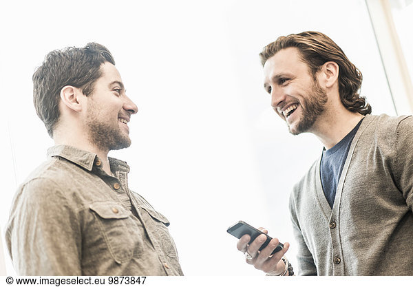 Two men smiling  one holding a smart phone.