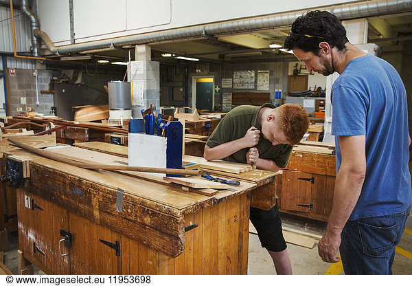 Two men standing at a workbench in a boat-builder's workshop  working on wooden joint.