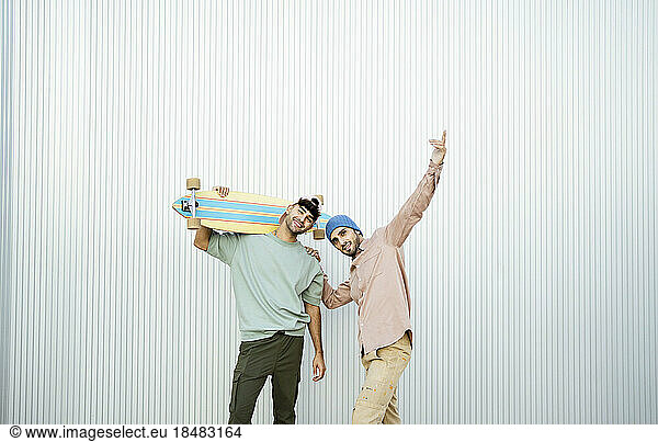 Two men standing with longboard in front of white wall