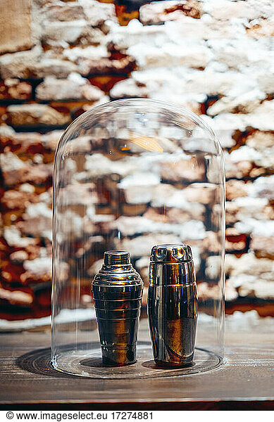Two metallic cocktail shakers under glass cover