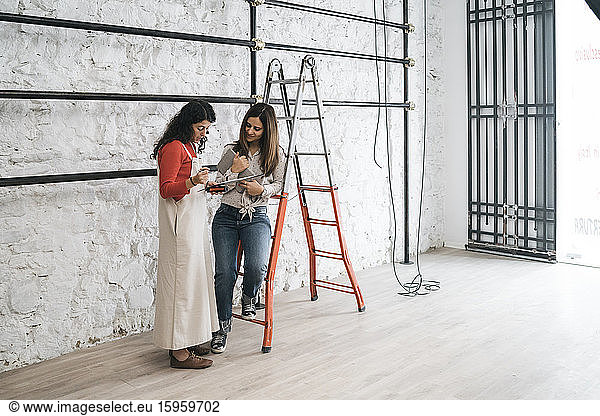 Two mid adult women checking blueprint in their new shop