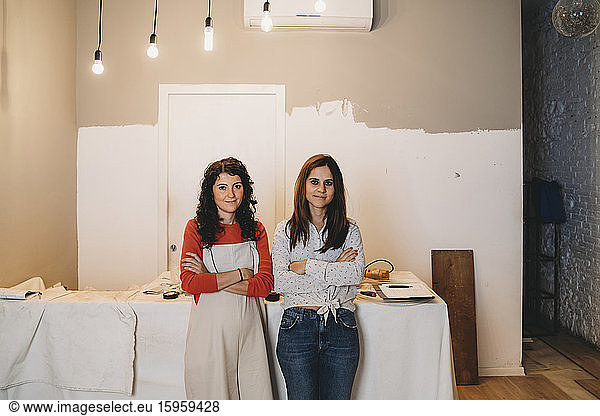 Two mid adult women leaning against table while painting in their new shop  portrait