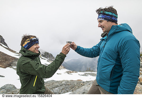 Two mountaineers toasting shot glasses in the mountains.