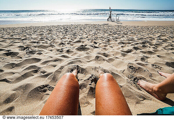 two pair of women's legs in the sand on the beach