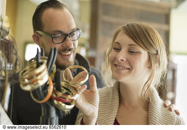 Two people  a man and woman looking at the objects displayed on a mannequin hand  antique jewellery and objects.