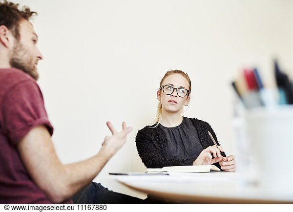Two people at a meeting  a man gesticulating and a woman listening.