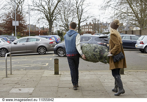 Two people carrying a netted Christmas tree to the car park.