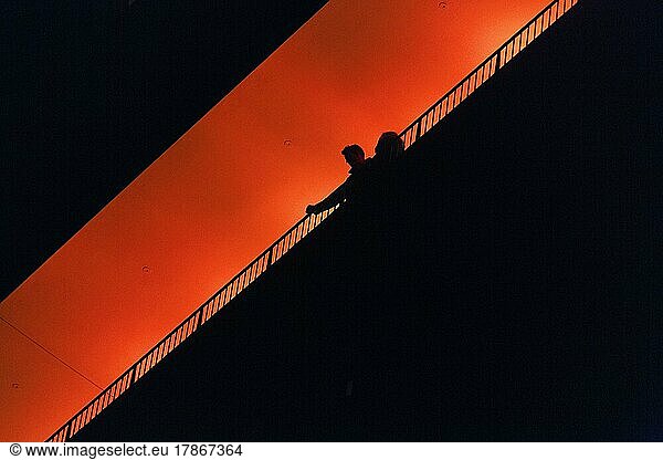 Two people  couple standing on observation deck Plaza  enjoying view  silhouettes in the darkness  illuminated orange  Elbe Philharmonic Hall in the evening  view from below  text free space  Hamburg  Germany  Europe
