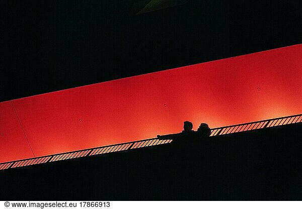 Two people  couple standing on observation deck Plaza  looking down  silhouettes in the darkness  illuminated orange  Elbe Philharmonic Hall in the evening  view from below  text free space  Hamburg  Germany  Europe
