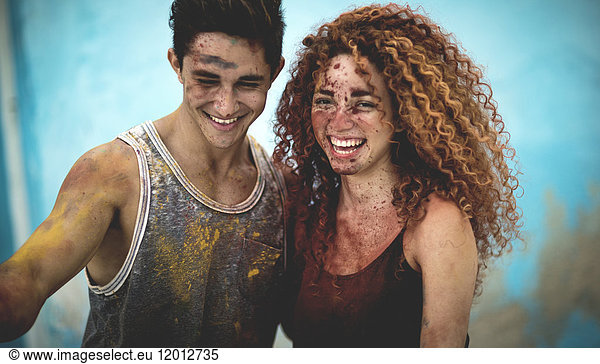 Two people covered in paint splatter and smiling.