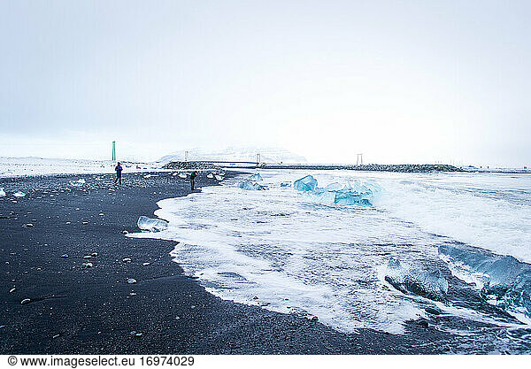 Two people explore black-sand Diamond Beach in Iceland during winter