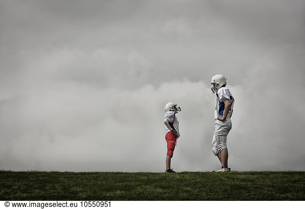 Two people facing each other  one very tall football player  and one much shorter person looking up  hands on hips.