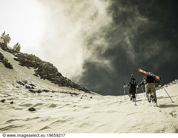 Two people hiking up a snow slope with ski gear.