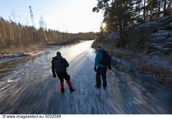 Two people ice skating on frozen creek