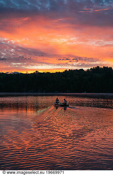 Two people in fishing boat heading across a lake at sunrise.
