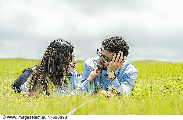Two people in love lying on the grass looking at each other  A couple lying on the grass looking at each other  Young couple in love lying on the grass touching each other's faces