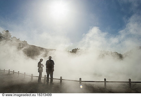 Two people in rising mist at a thermal pool site