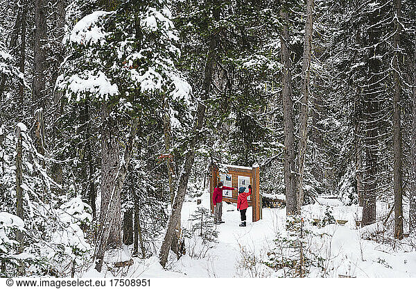 Two people in the snow looking at a notice board in winter resort.
