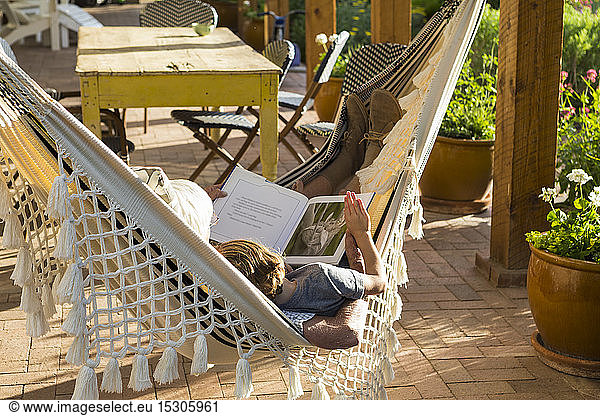 Two people lying in a hammock on a porch reading.