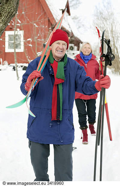Two people outdoors carrying skis