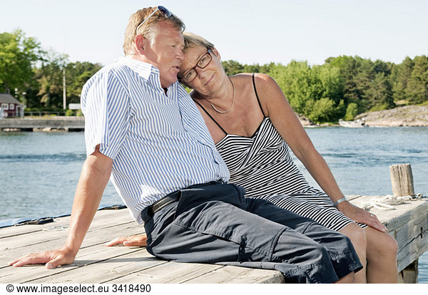 Two people sitting on pier by the water