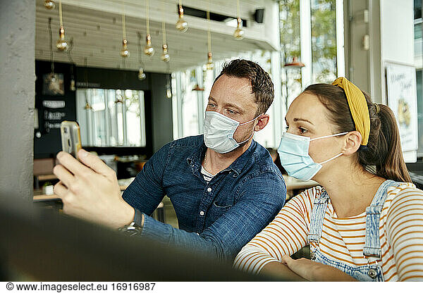Two people wearing face masks  using a smart phone  waving during a face time call.
