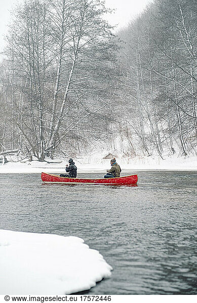 Two persons paddling in a red wooden canoe on the snowy river.