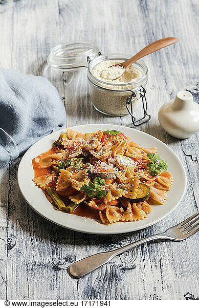Two plates of bow tie pasta with vegetables and vegan Parmesan