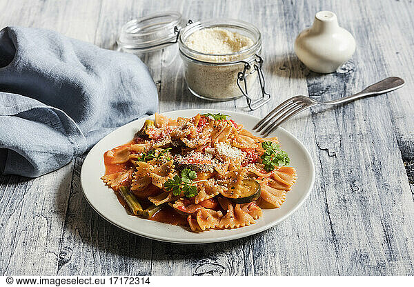 Two plates of bow tie pasta with vegetables and vegan Parmesan