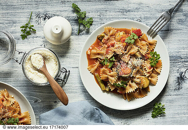 Two plates of bow tie pasta with vegetables and vegan Parmesan