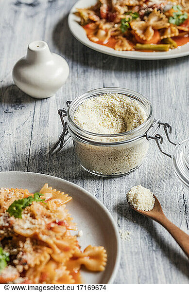 Two plates of vegan pasta with vegetables and jar of shredded vegan Parmesan cheese