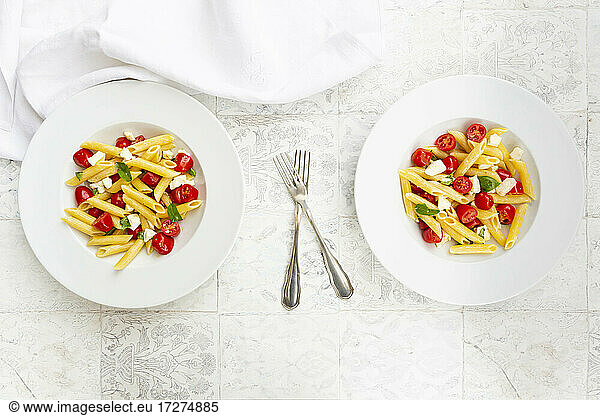 Two plates of vegetarian pasta with mozzarella  cherry tomatoes and basil
