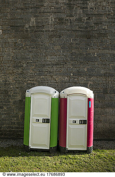 Two portable toilets standing side by side in front of brick wall