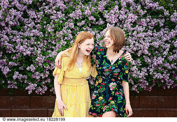 Two pretty teen girls laughing together  surrounded by lilac blooms.