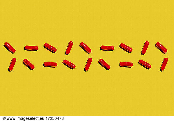 Two rows of red medicine capsules laid against yellow background