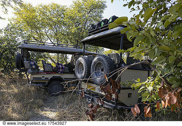 Two safari vehicles parked in the shade of trees.