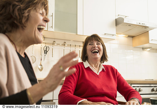 Two senior women talking and laughing in kitchen