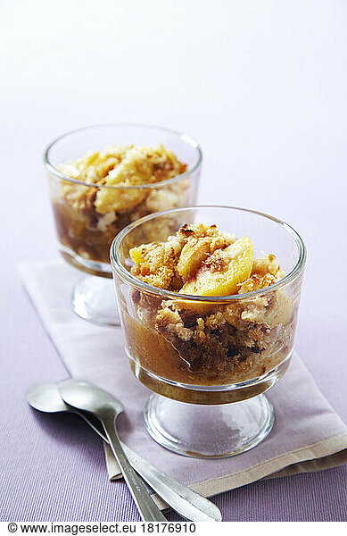 Two servings of apple pear crisp in glasses with spoons on a purple background