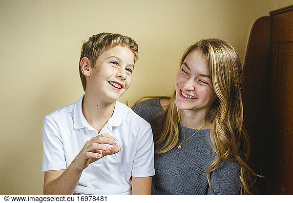 Two siblings sit together on a wood bench laughing with joy indoors