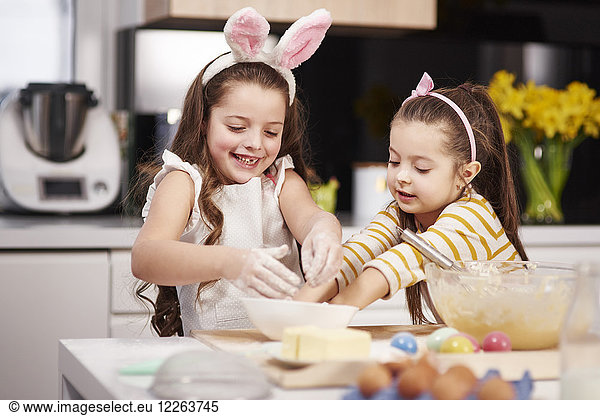Two sisters having fun baking Easter cookies in kitchen together