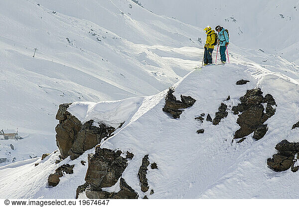 Two skiers talking about their line before dropping in the face
