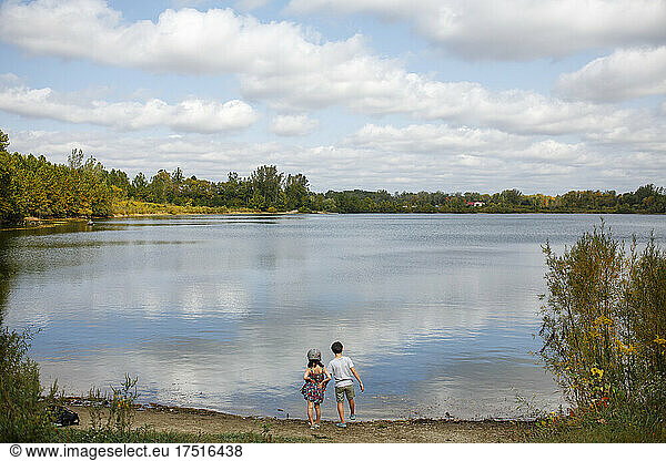 Two small children stand by lake on sunny summer day