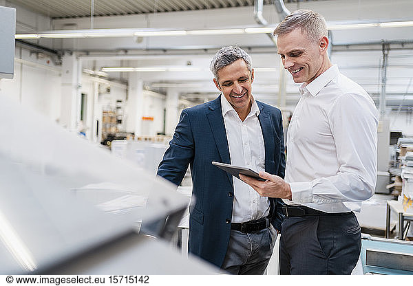 Two smiling businessmen looking at tablet in a factory