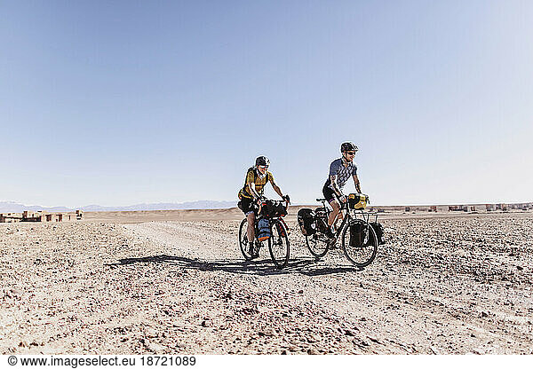 Two smiling caucasian cyclists ride a desert dirt road in Morocco