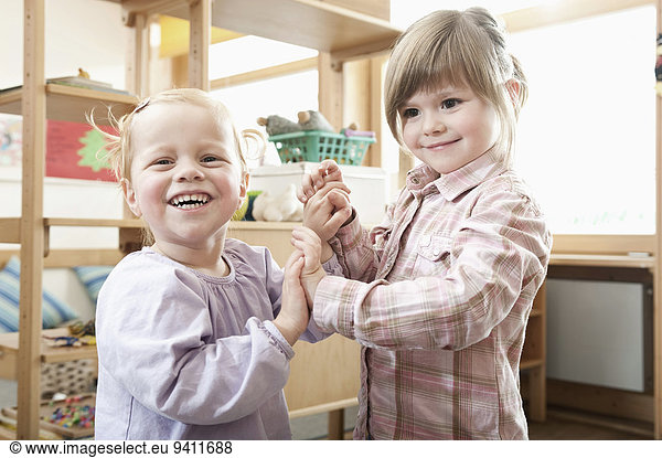 Two smiling little girls holding hands in kindergarten