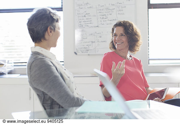 Two smiling women talking in office  whiteboard in background