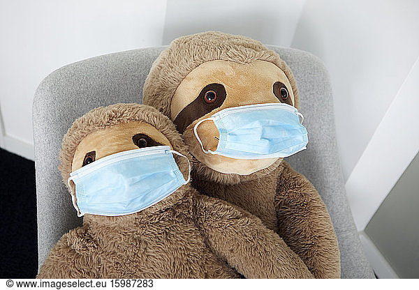 Two soft toys on arm chair with protective masks