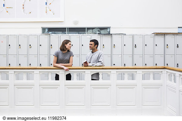 Two students (16-17) by railing in front of lockers